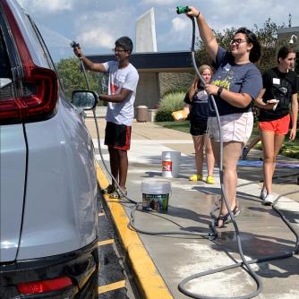 Teenagers spaying water hoses onto a soapy car during a car wash event