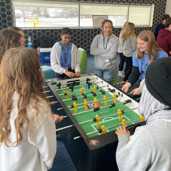 Teenagers are gathered around a foosball table and play a game together